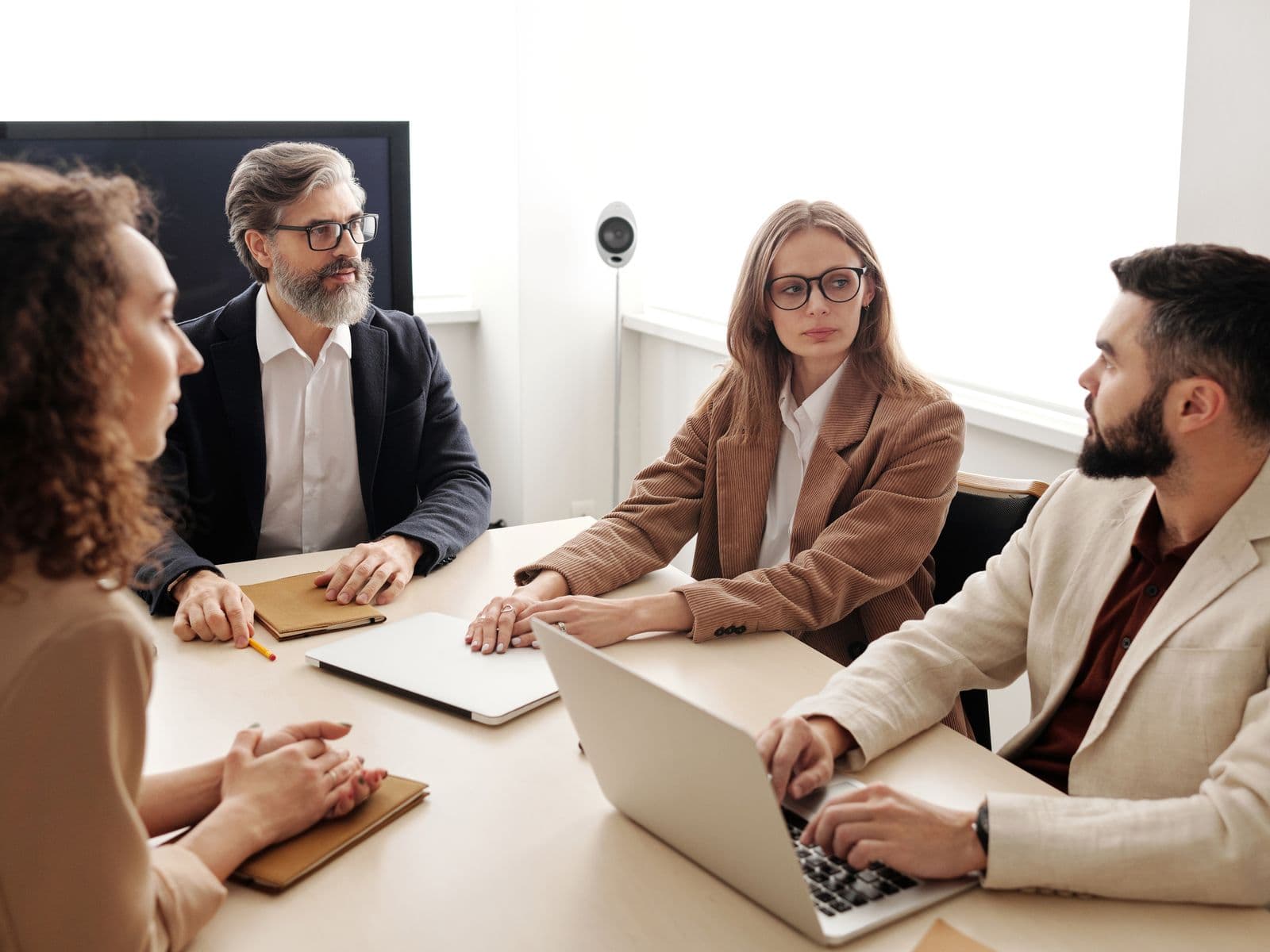 Quatre collaborateurs en veste échangeant autour d’une table de réunion, ordinateurs portables ouverts, dans une salle lumineuse
